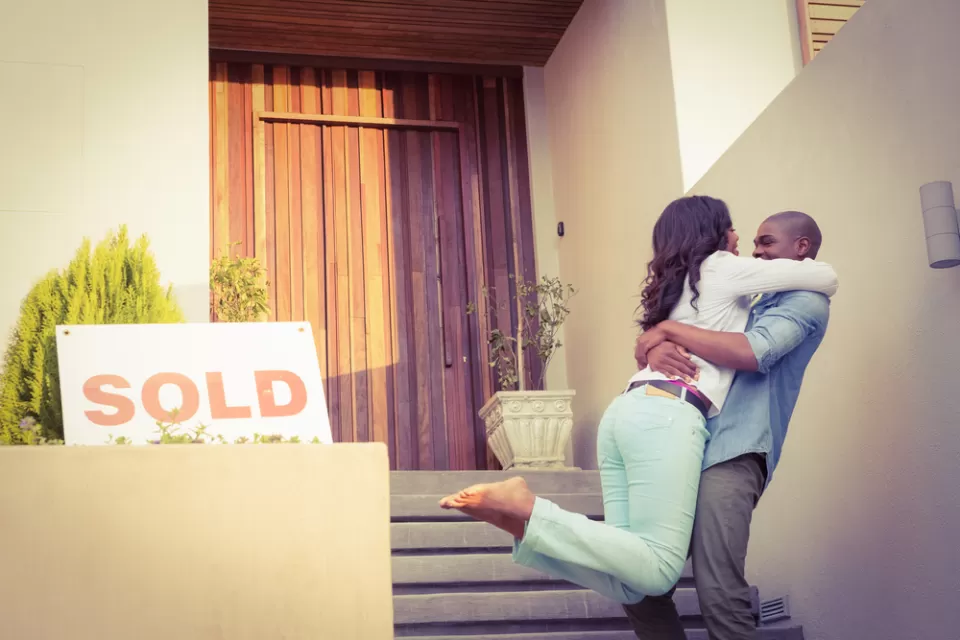 Couple embracing happily in front of home with "SOLD" sign
